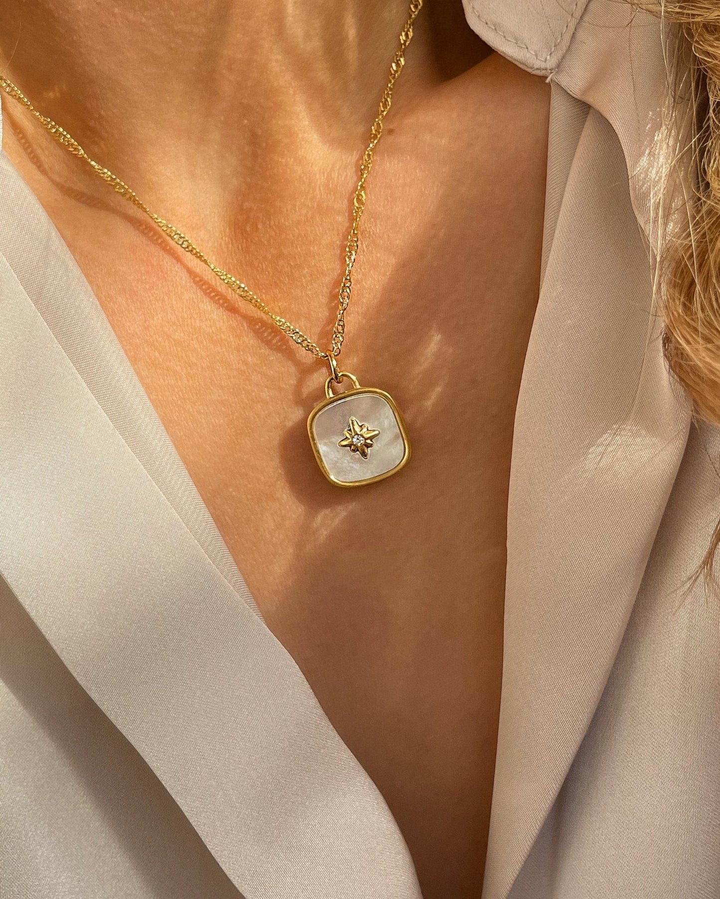 18k Vergoldete Edelstahlkette mit Perlmutt Design Anhänger, getragen mit einer cremefarbener Bluse. Wasserfest, hypoallergen und besonderes im Design.