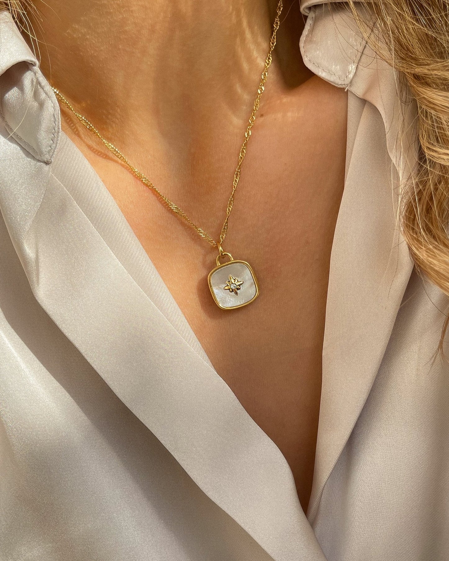 18k Vergoldete Edelstahlkette mit Perlmutt Design Anhänger, getragen mit einer cremefarbener Bluse. Wasserfest, hypoallergen und besonderes im Design.