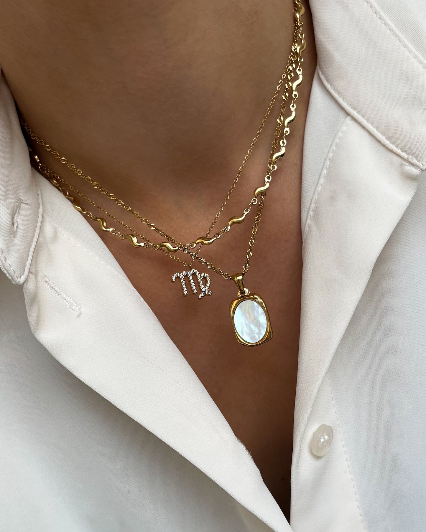 Drei goldene Halsketten mit Sternzeichen Design, schimmernder Muschelperle und Wellendesign, getragen mit weißer Bluse.