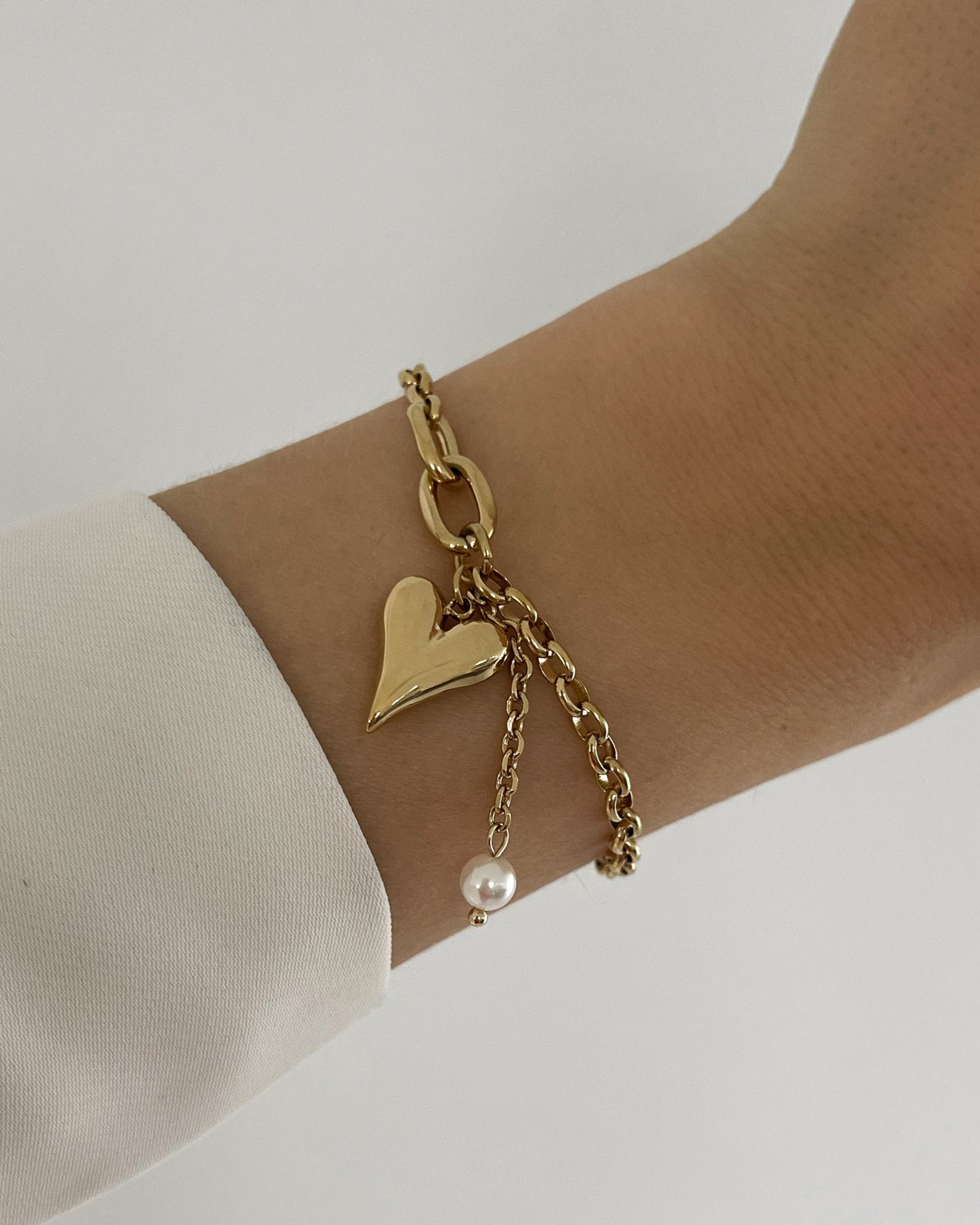 Goldenes Armband mit liebevollem Herz Anhänger und kleinen Perle, getragen am Handgelenk.