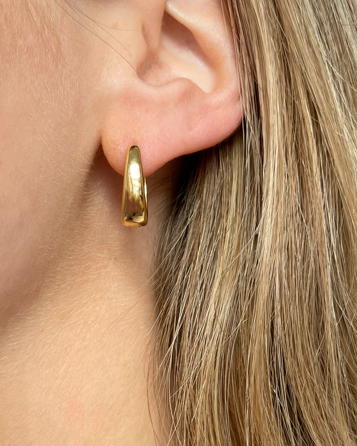 Ovale wasserfeste Edelstahl Hoops in gold, getragen am Ohr.