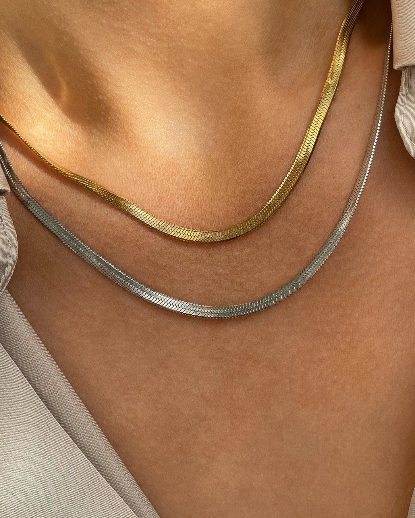 Zwei Vergoldete Edelstahl Halsketten mit Schlangen Designs, getragen mit cremefarbener Bluse. Wasserfest und hypoallergen.