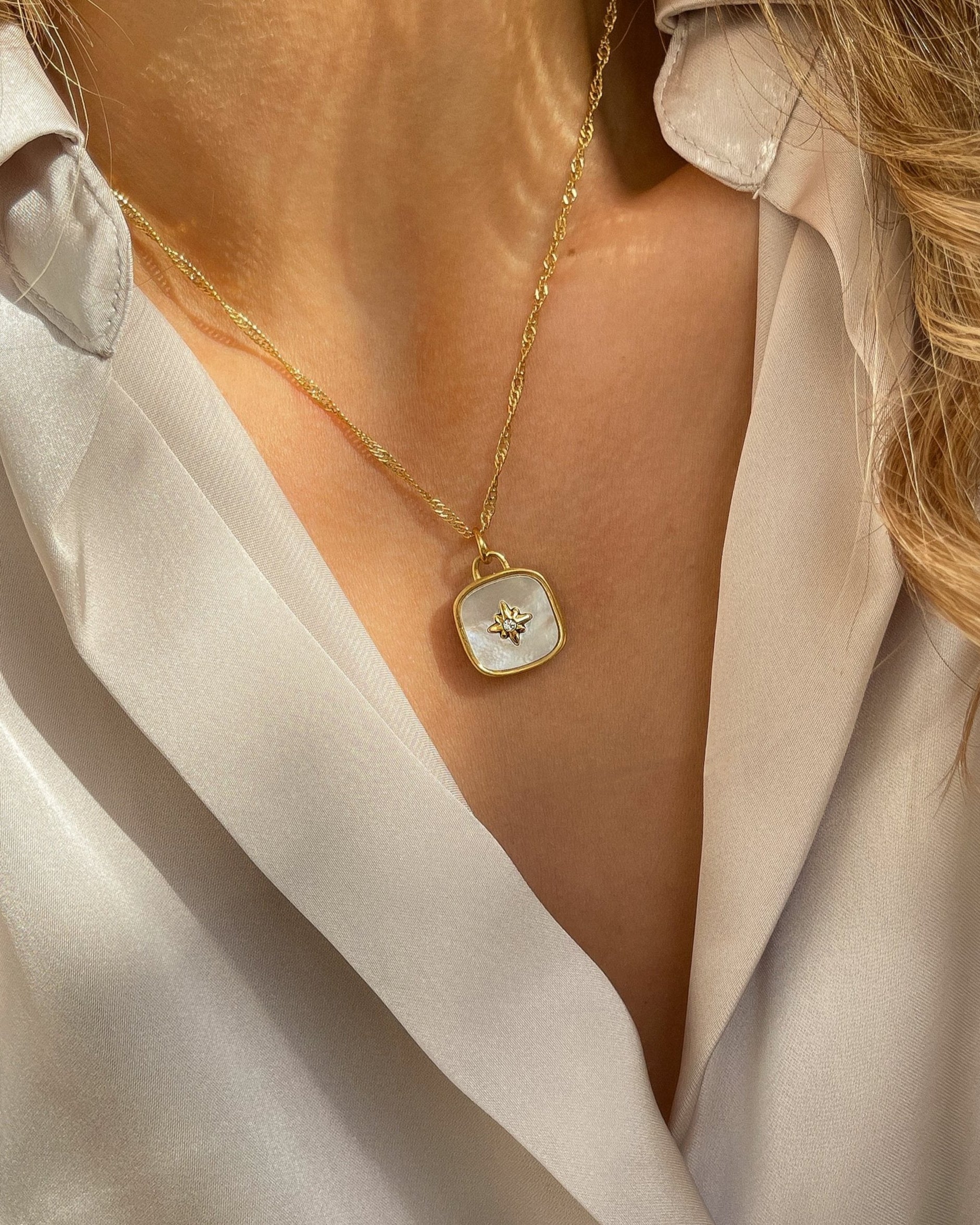 18k Vergoldete Edelstahlkette mit Perlmutt Design Anhänger, getragen mit einer cremefarbener Bluse. Wasserfest, hypoallergen und besonderes im Design.