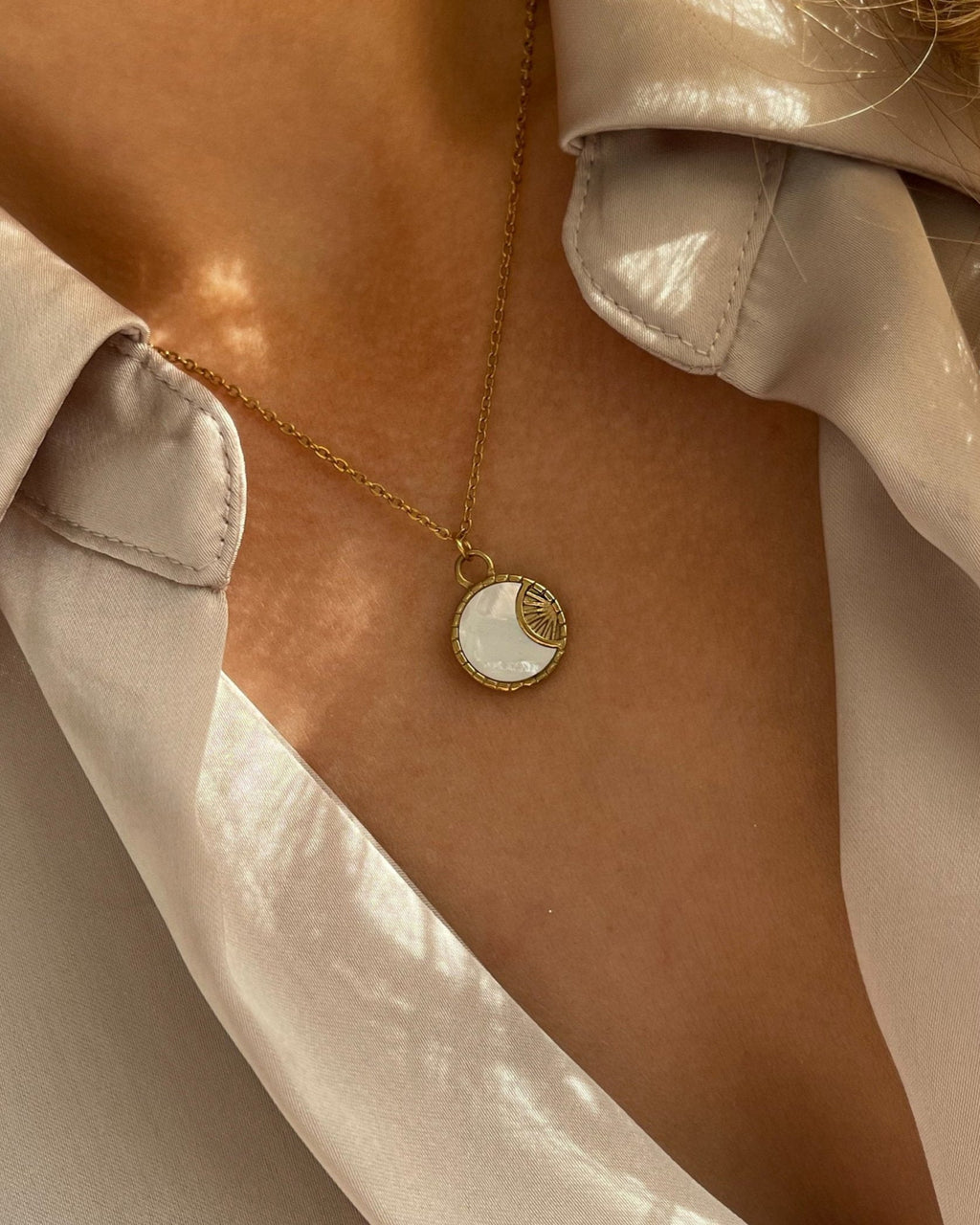 Goldene Halskette mit rundem schimmernden Plättchen, getragen mit beiger Bluse.
