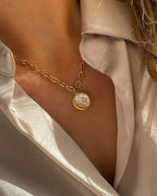 Grobe Halskette mit einem Anhänger aus schimmernder Muschelperle und Details in Mond und Sternform, getragen mit einer beigefarbenen Bluse.