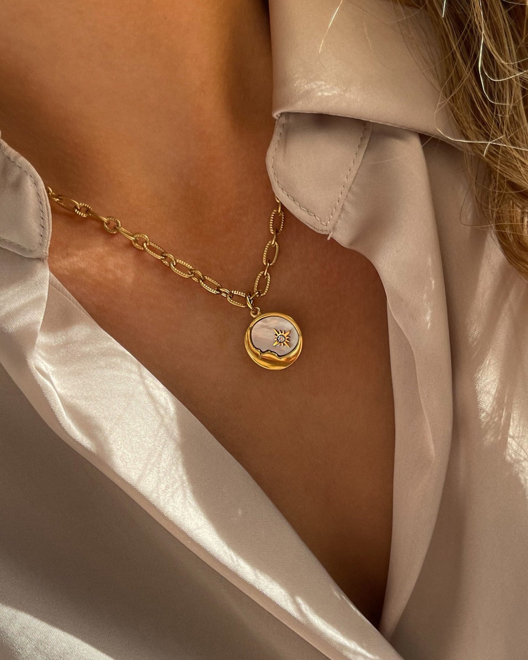 Grobe Halskette mit einem Anhänger aus schimmernder Muschelperle und Details in Mond und Sternform, getragen mit einer beigefarbenen Bluse.
