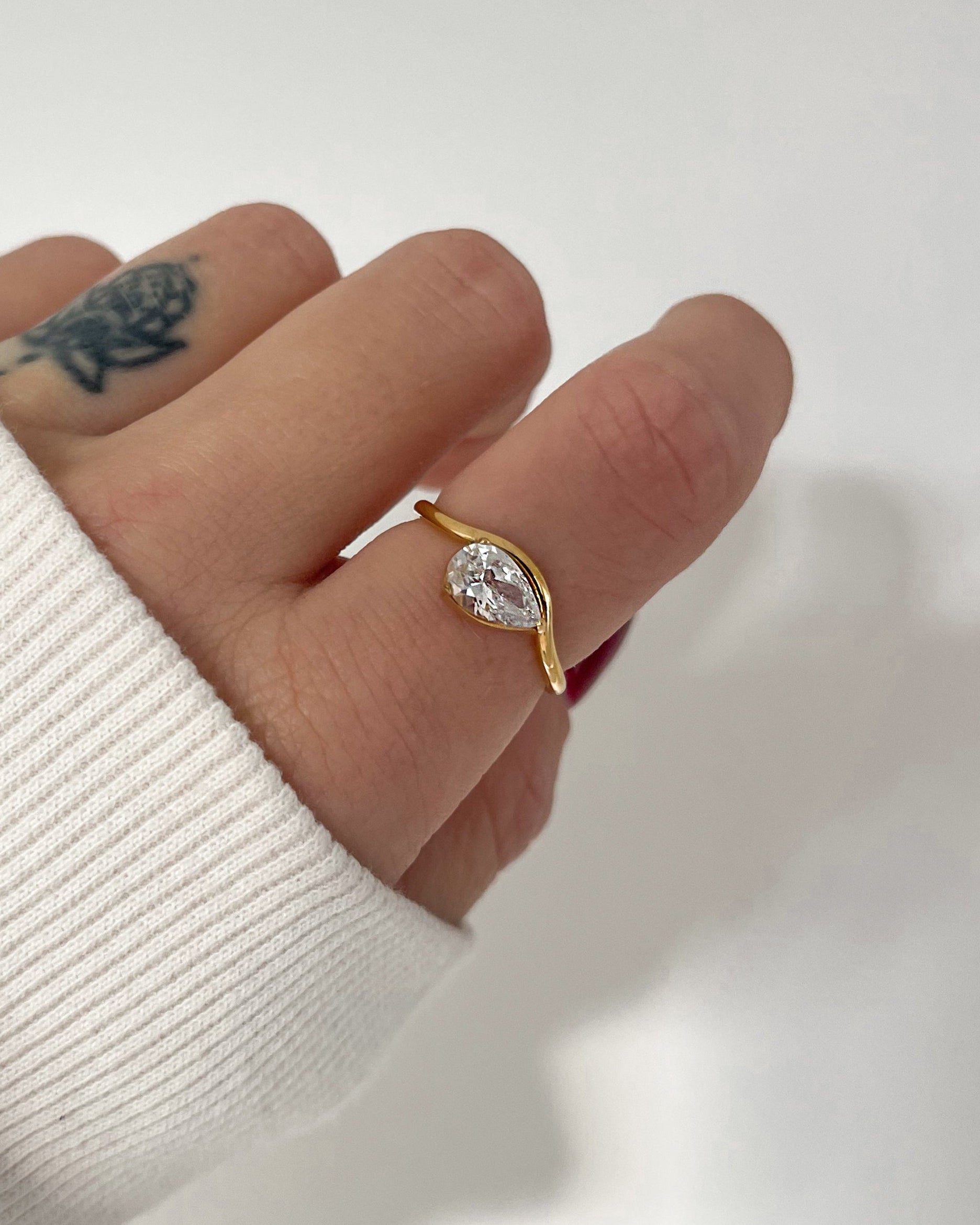 Wasserfester, goldener Edelstahl Ring geschwungen mit einem Tropfen Zirkonia, getragen am Finger.