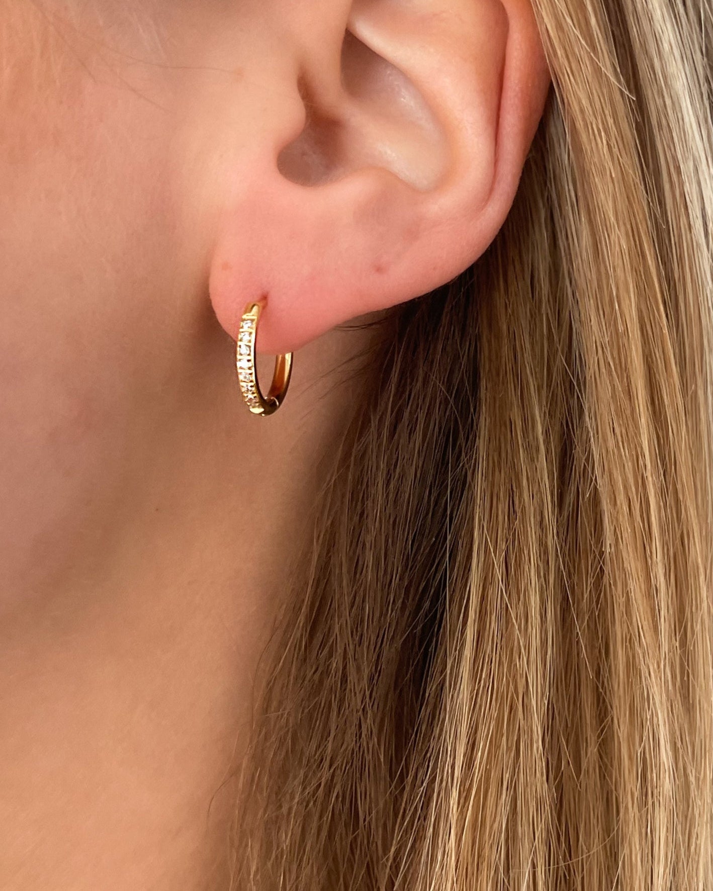 Wasserfeste Edelstahl Hoops mit Zirkonia Steinen besetzt in gold, getragen am Ohr.