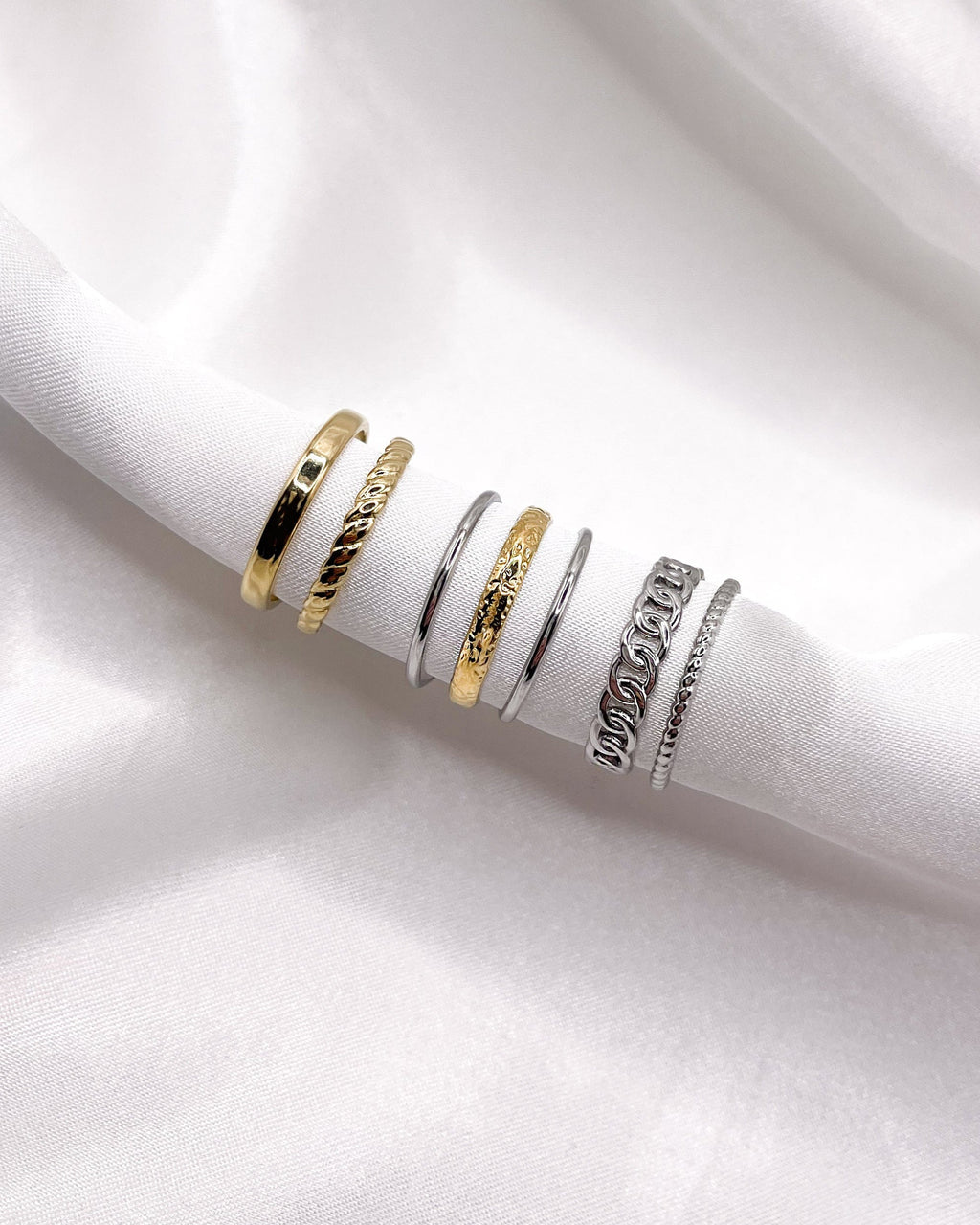 Dreilagiger Edelstahlring in Bicolor auf weißem Stoff mit zwei anderen Ringen.