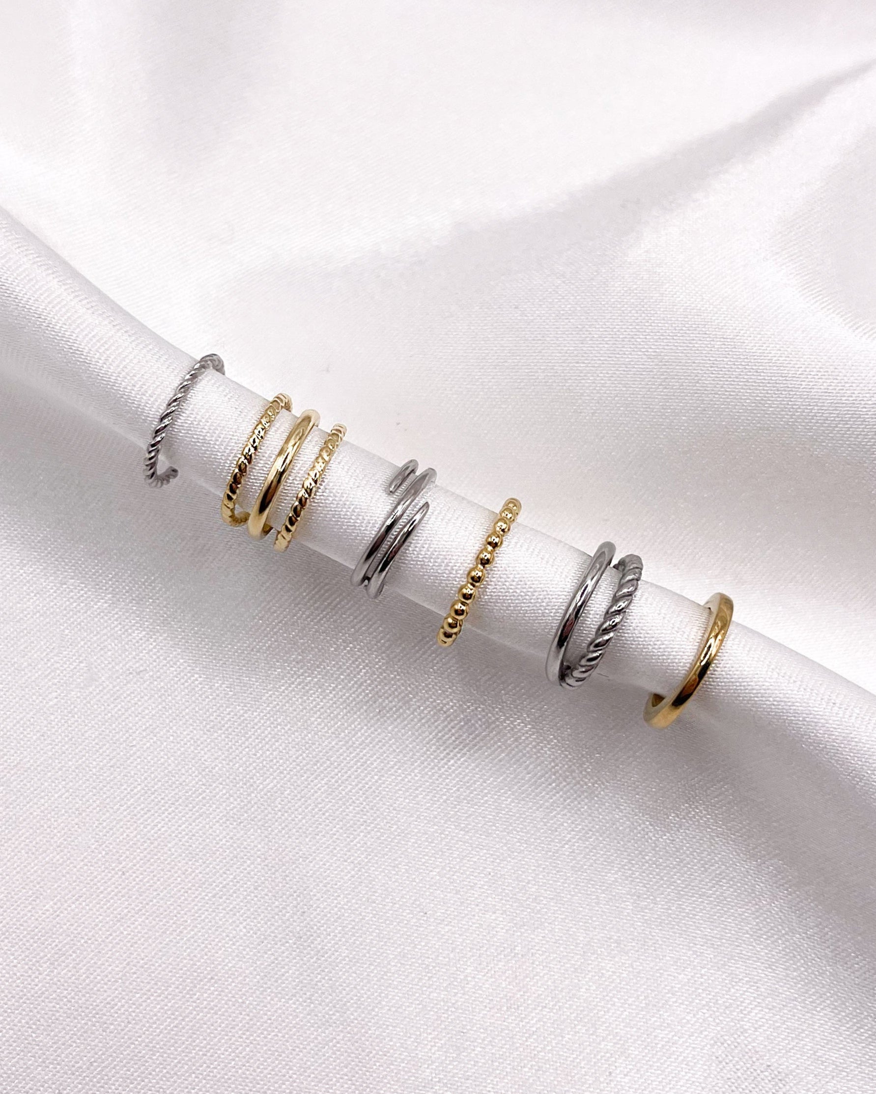 Verschiedene silberne und goldene Earcuffs auf weißem Satinstoff.