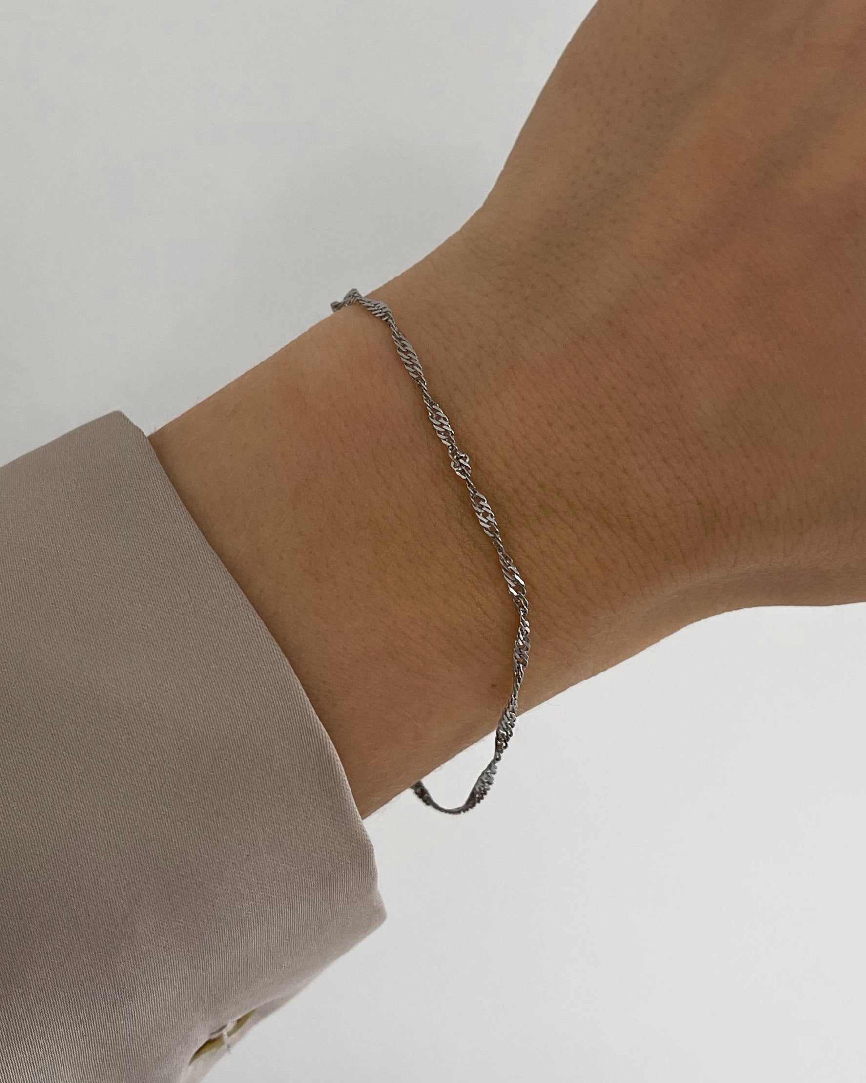 Feines, wasserfestes Edelstahl Armband mit gedrehtem Design, getragen am Handgelenk in silber.