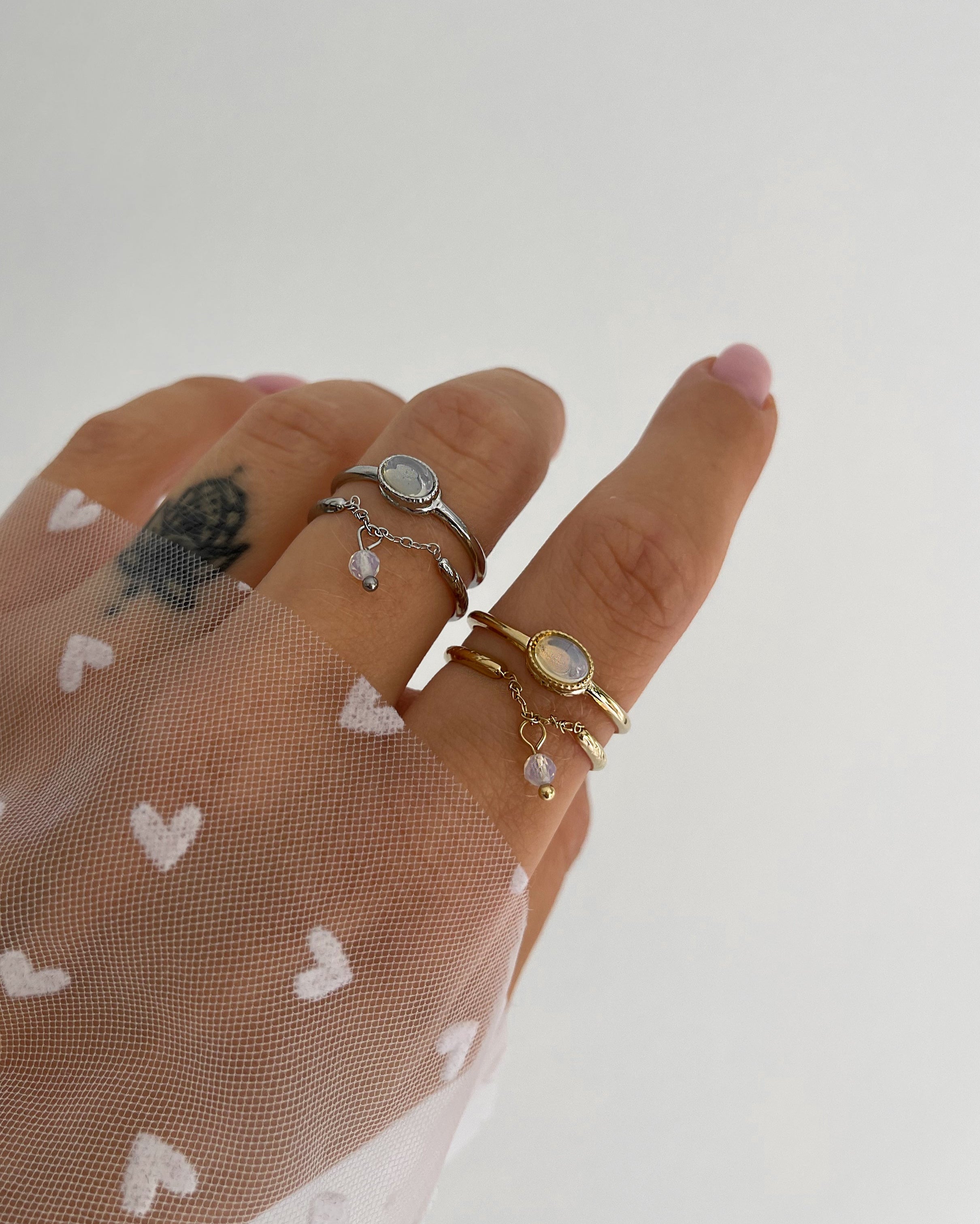 Doppellagiger Ring mit schimmerndem Detail und Kettendesign, getragen am Finger.