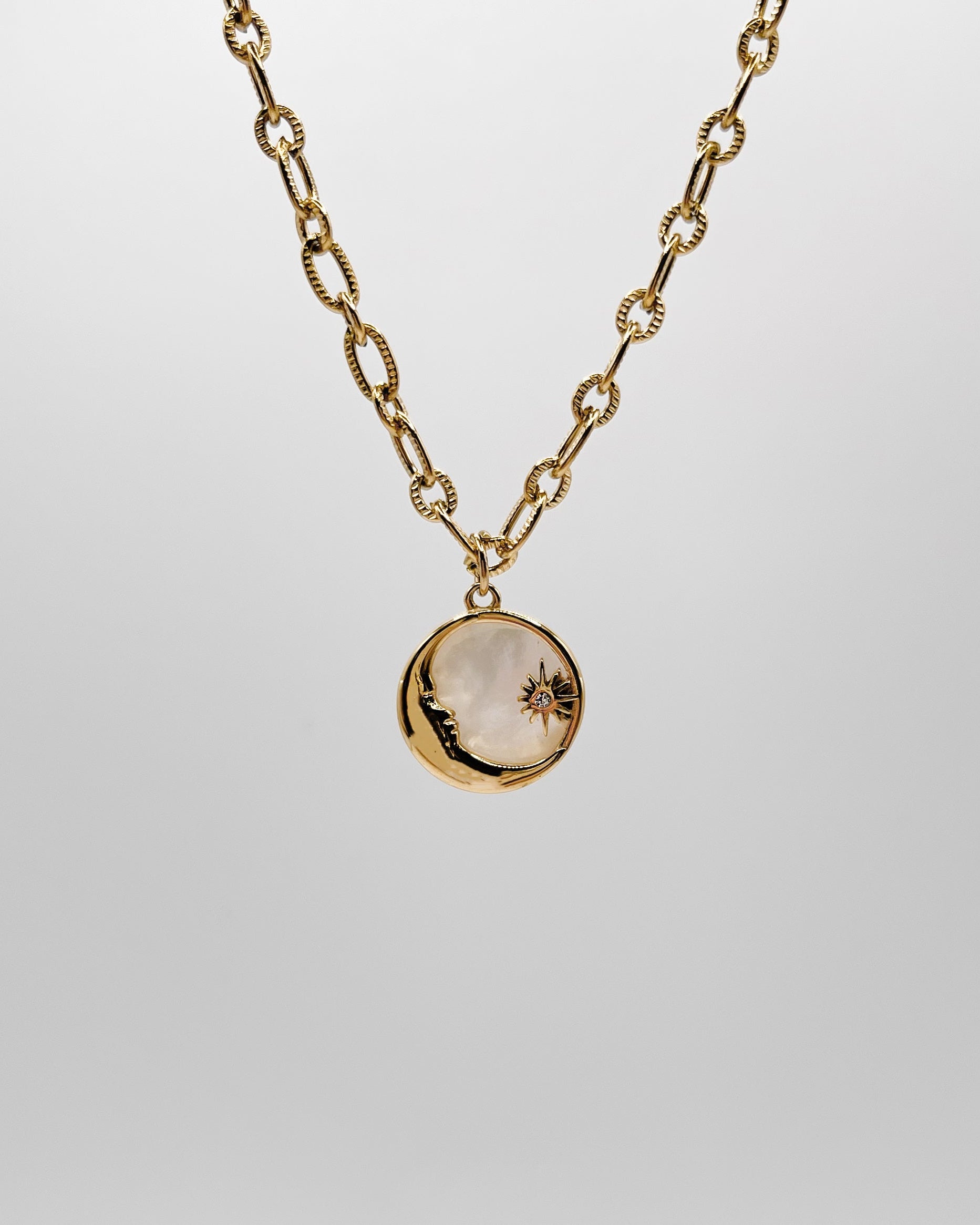 Grobe Halskette mit einem Anhänger aus schimmernder Muschelperle und Details in Mond und Sternform.