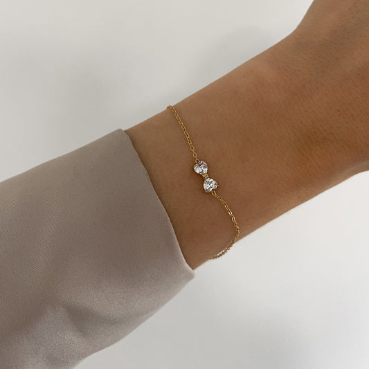Armband ''Little Bowty'' besticht durch sein feines Schleifen Design aus zwei herzförmigen Zirkonia Steinen, getragen am Handgelenk in gold.