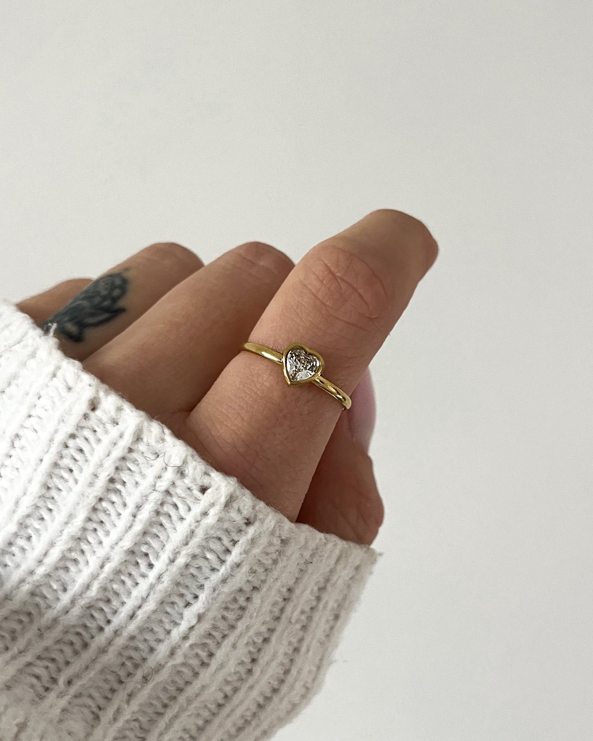 Schlichter, verstellbarer Ring mit einem Herzförmigen Zirkonia Stei, getragen am Finger.