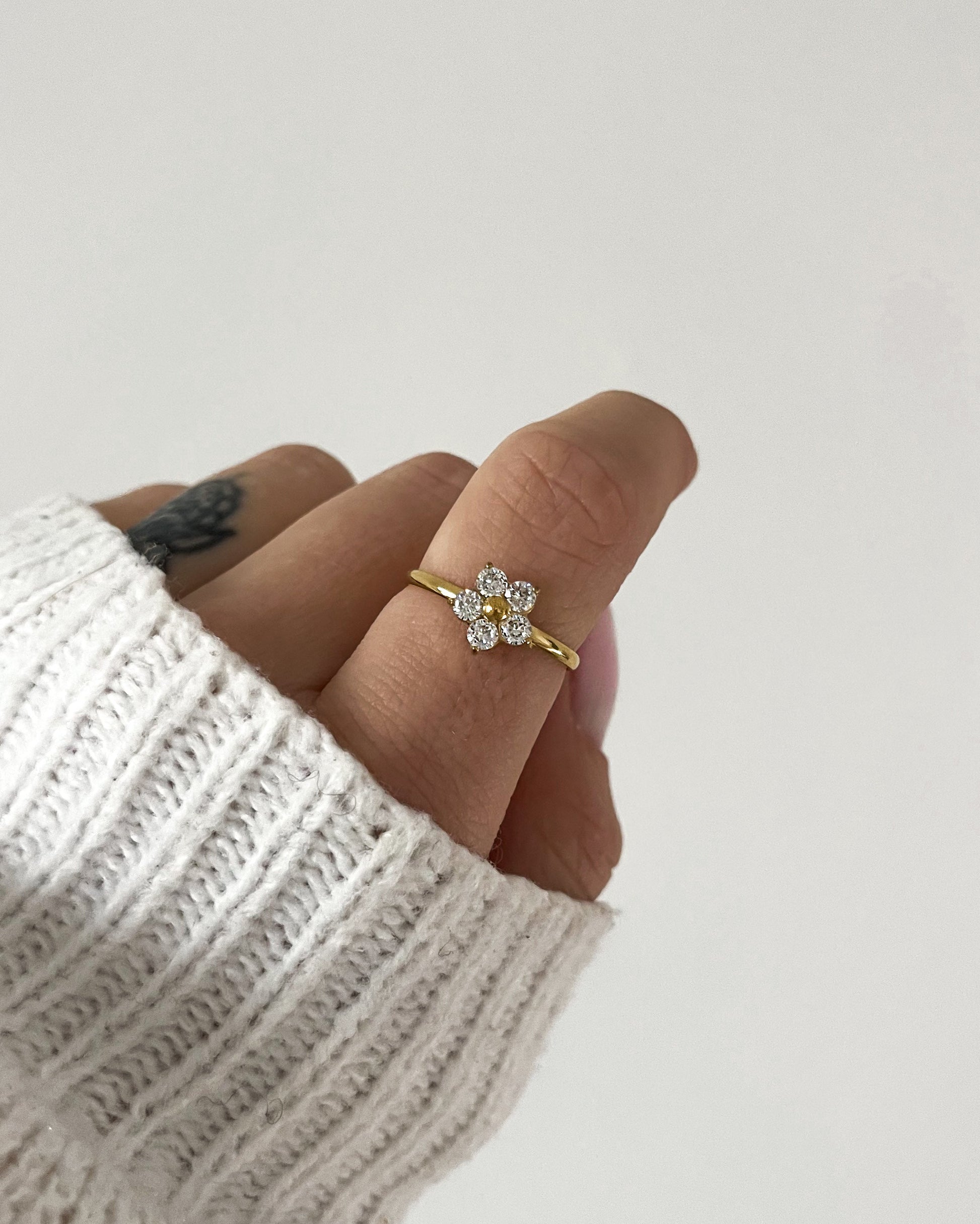 Goldener Ring mit einem Blumendesign aus Zirkonia Steinen, getragen am Finger.