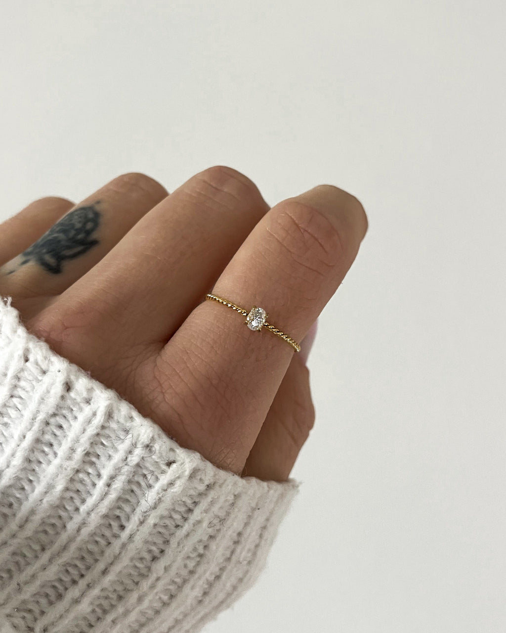 Goldener Ring mit einem feinen gedrehten Design und einem kleinen runden Zirkonia, getragen an Finger.