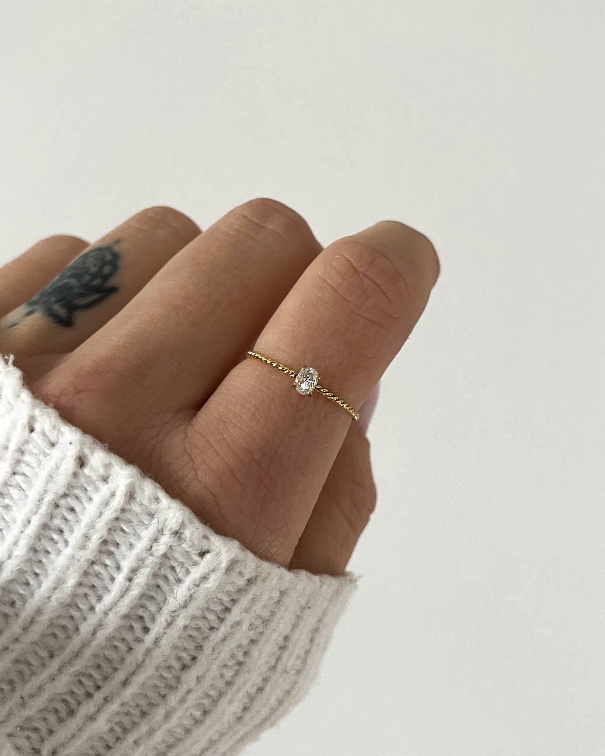 Goldener Ring mit einem feinen gedrehten Design und einem kleinen runden Zirkonia, getragen an Finger.