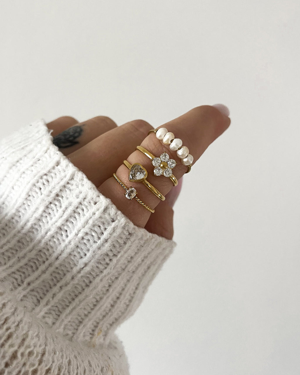 Vier goldene Ringe am Finger, in Blumen, Herz und Perlendesign.