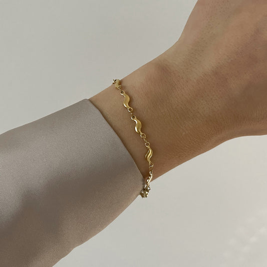Goldenes Armband mit Design in Wellenform, getragen am Handgelenk.