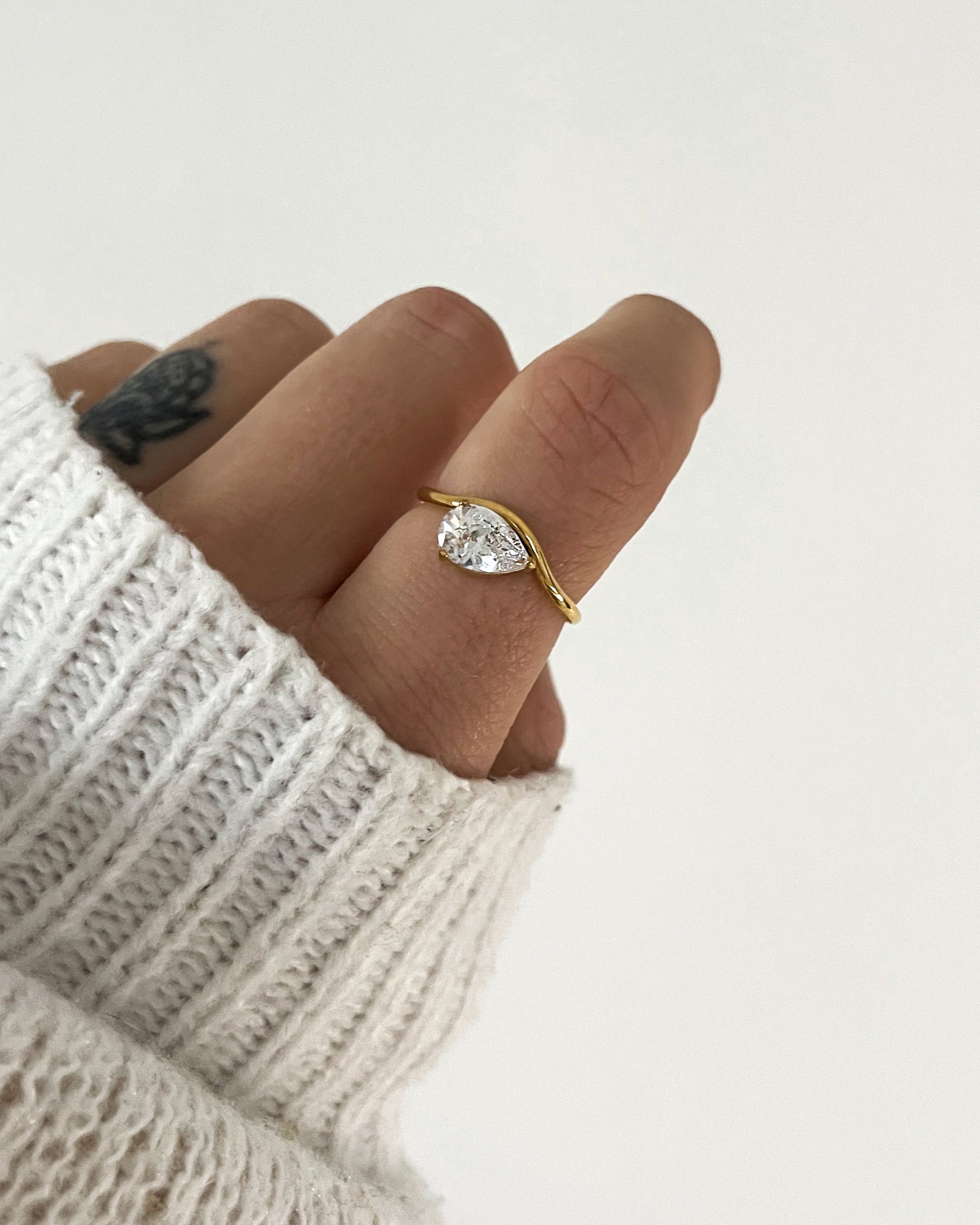 Wasserfester, goldener Edelstahl Ring geschwungen mit einem Tropfen Zirkonia, getragen am Finger.