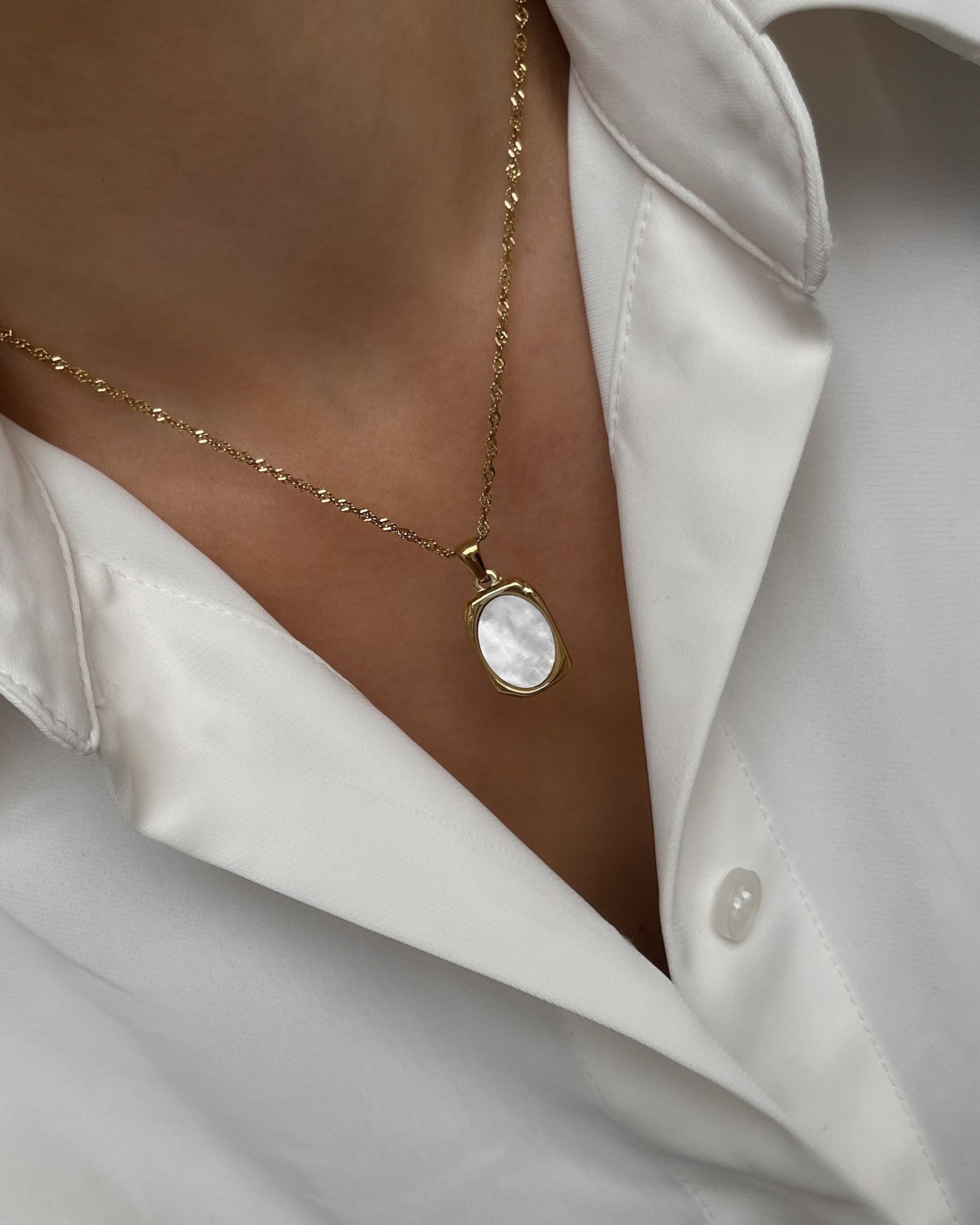 Goldene Halskette mit Ovalem Anhänger aus weißer Muschelperle, getragen mit weißer Bluse.