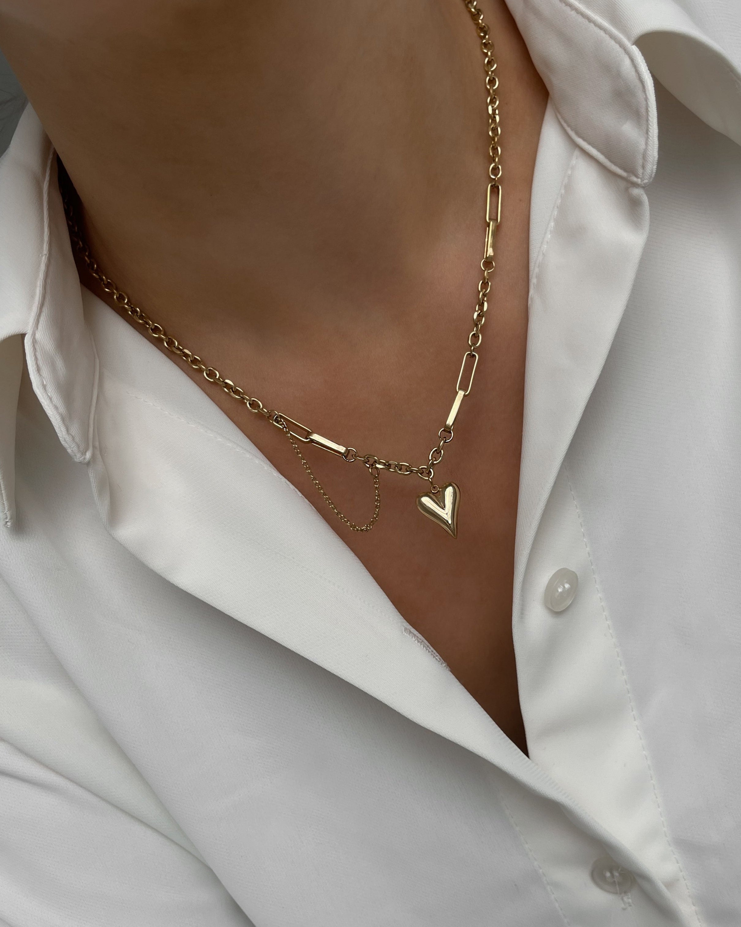 Vergoldete Edelstahlkette mit herzförmigem Anhänger, getragen mit einer weißen Bluse. 