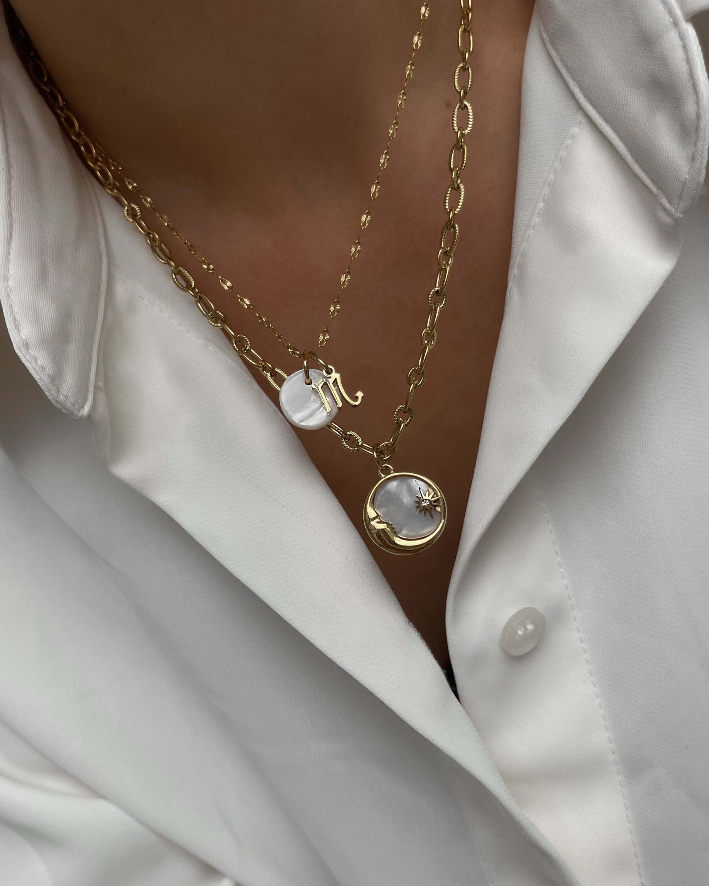 Zwei goldene Halskette mit einem Anhänger aus schimmernder Muschelperle und Details in Mond und Sternform, getragen mit einer weißen Bluse.