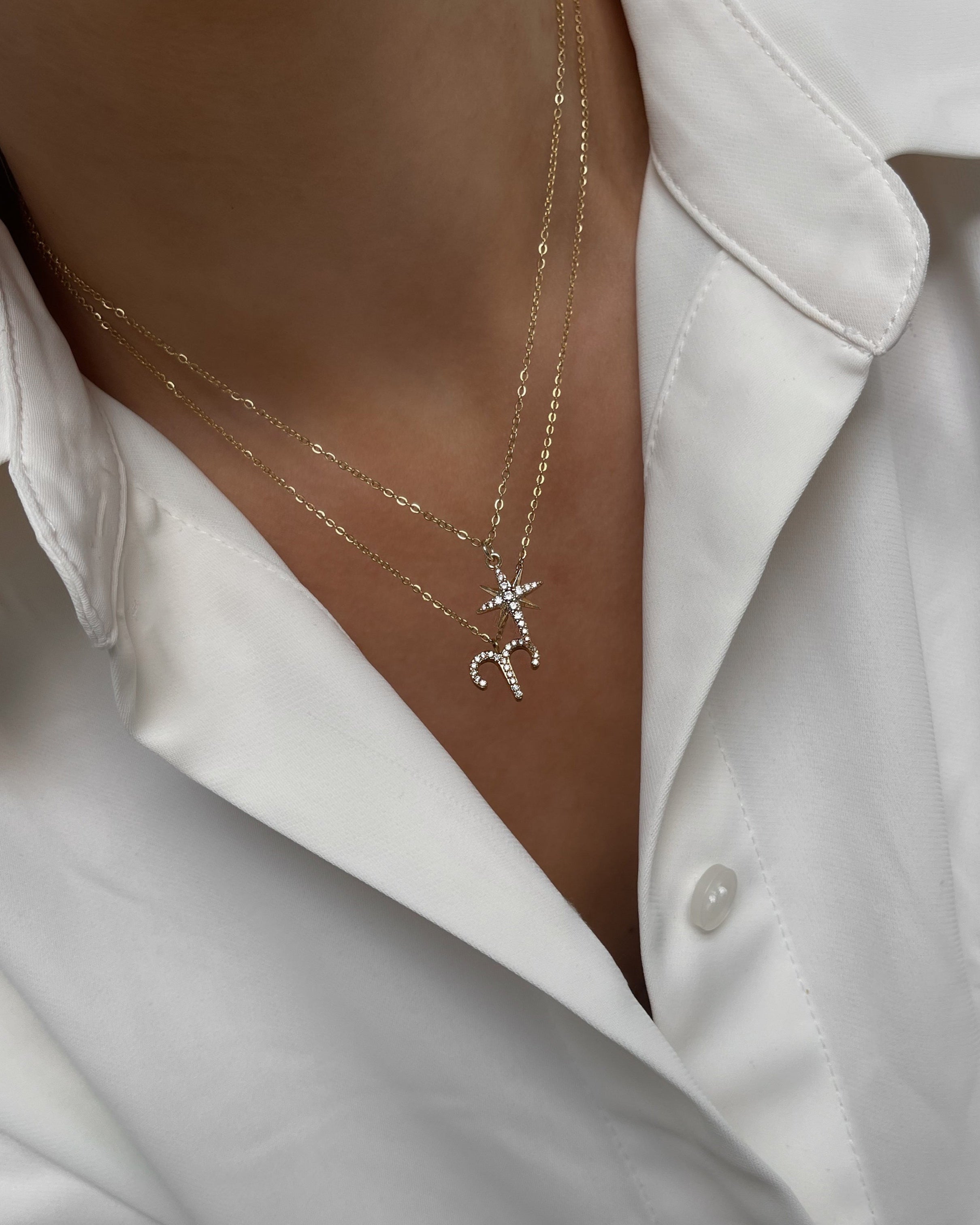 Goldene Halskette mit funkelndem Sternzeichen Anhänger aus Zirkonia Steinen, getragen mit weißer Bluse in Kombination mit einer weiteren Kette.