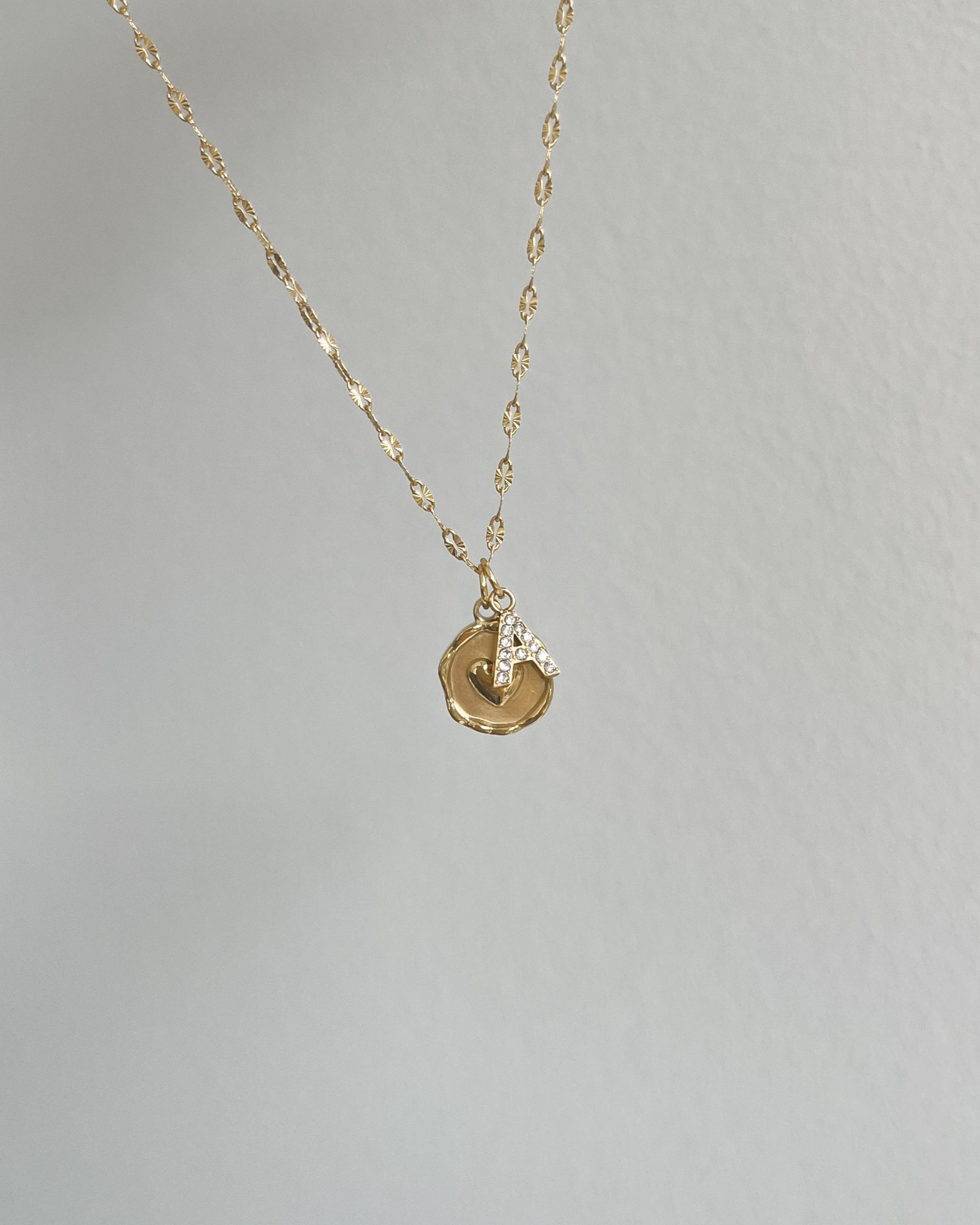 Runder Edelstahl Charm mit Herz in der Mitte an einer filigranen Kette mit Buchstaben Charm. Wasserfest und hypoallergen.