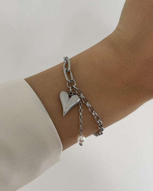 Silbernes Armband mit liebevollem Herz Anhänger und kleinen Perle, getragen am Handgelenk.

