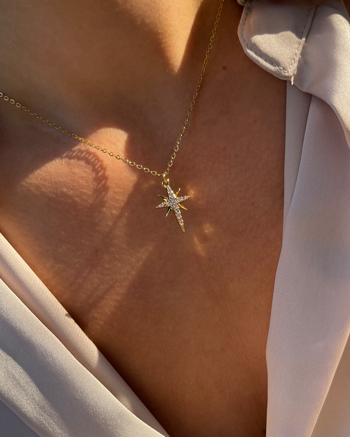Simple, filigrane Edelstahl Halskette mit funkelndem Anhänger aus Zirkonia Steinen in Sternform, getragen mit beiger Bluse. Wasserfest und hypoallergen.