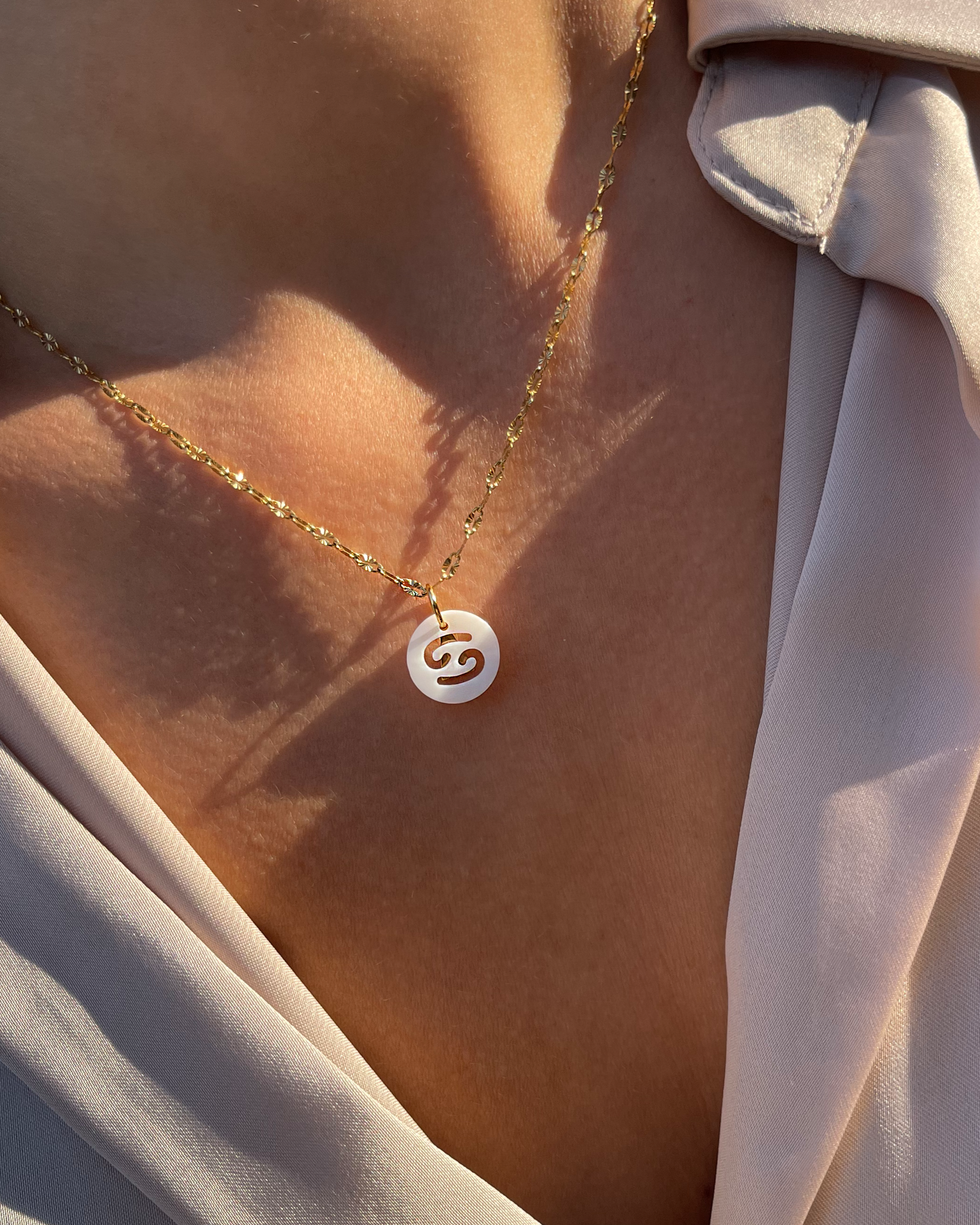 Weißer Charm mit ausgestanztem Sternzeichen Design, getragen an filigraner Halskette.