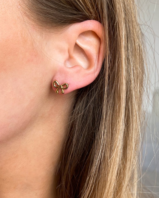 Goldene Ohrstecker mit einem zauberhaften Design mit einer kleinen Schleife. Getragen am Ohr.