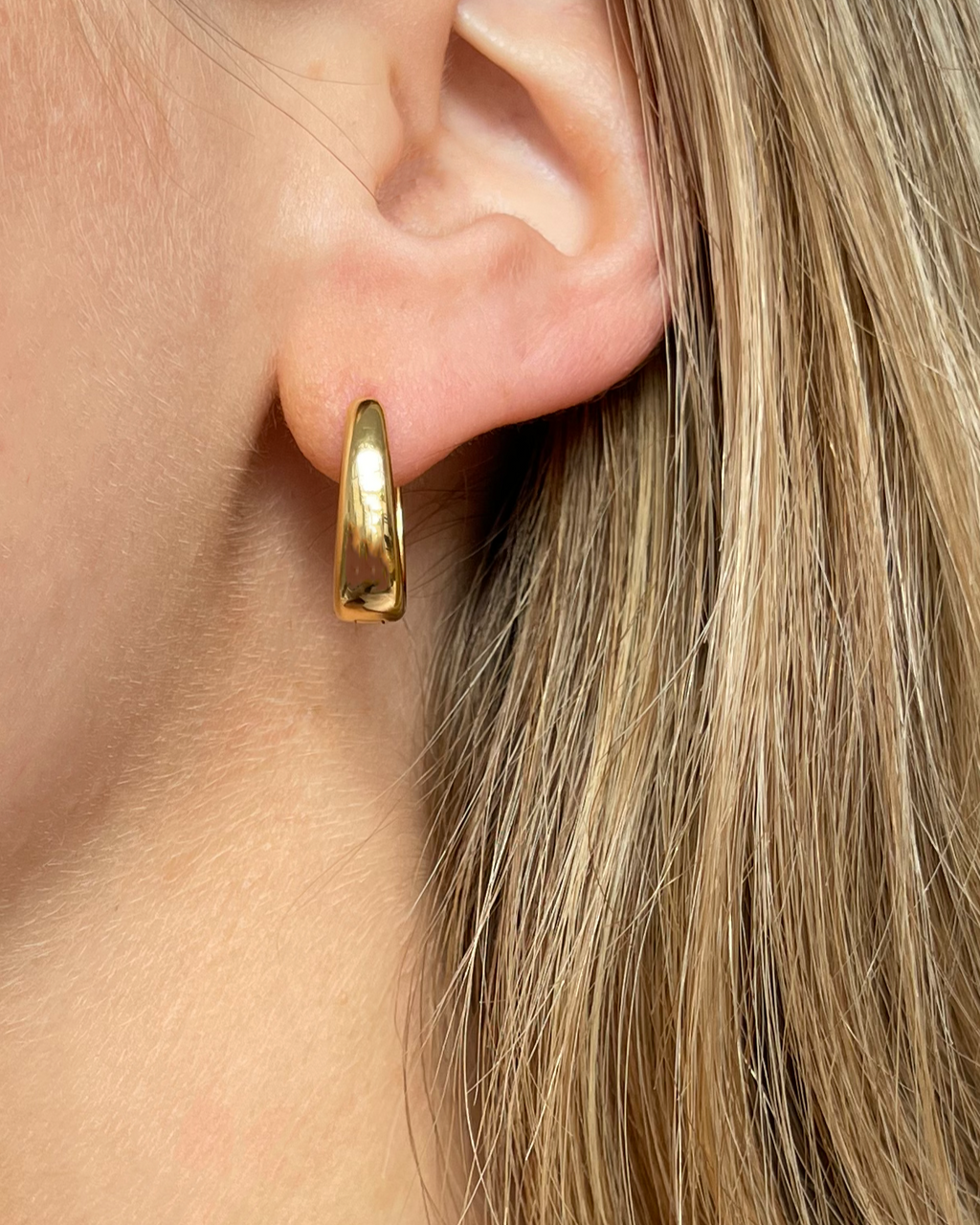 Ovale wasserfeste Edelstahl Hoops in gold, getragen am Ohr.