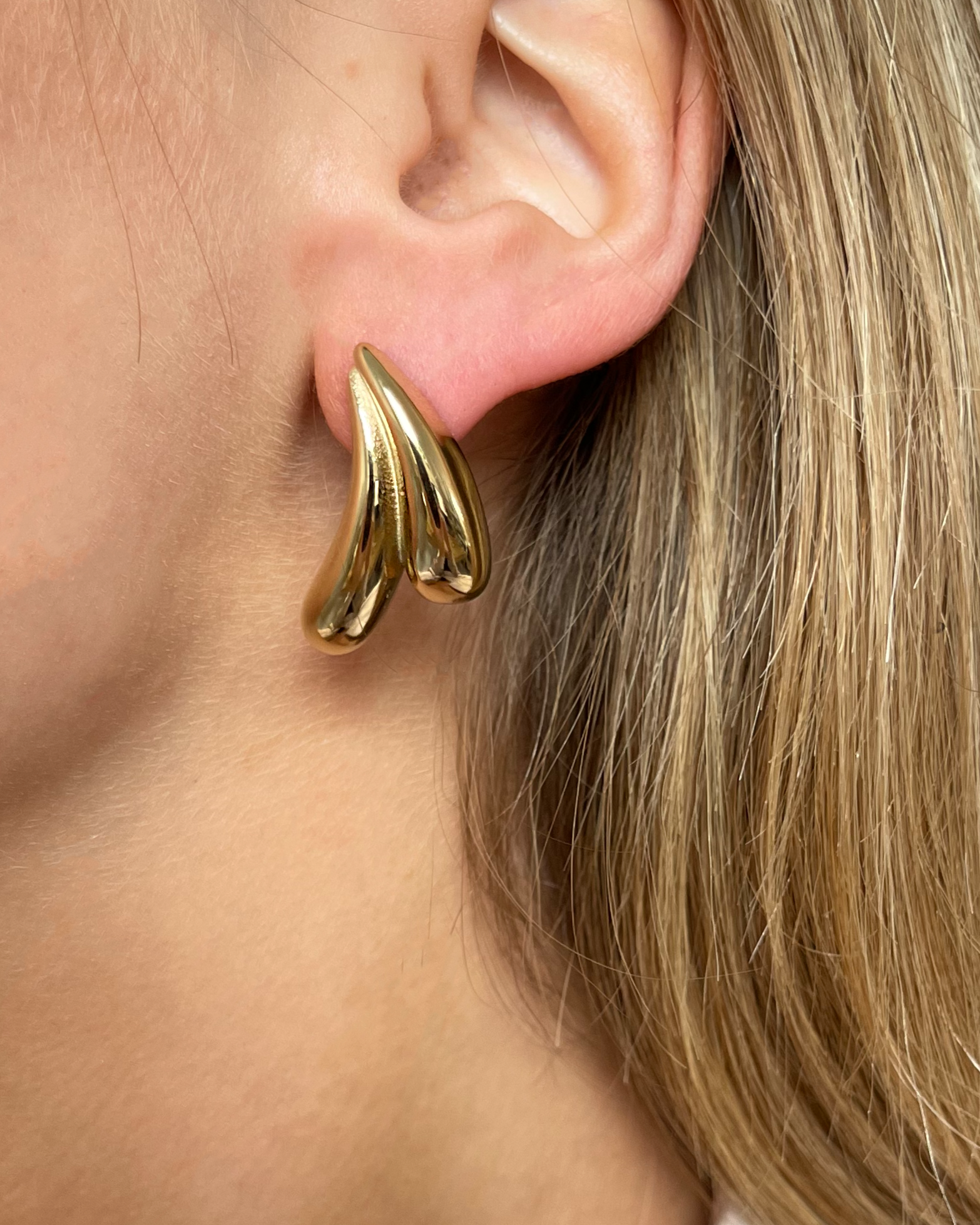 Wasserfeste Edelstahl Ohrstecker in wellenartigem Design in gold, getragen am Ohr.