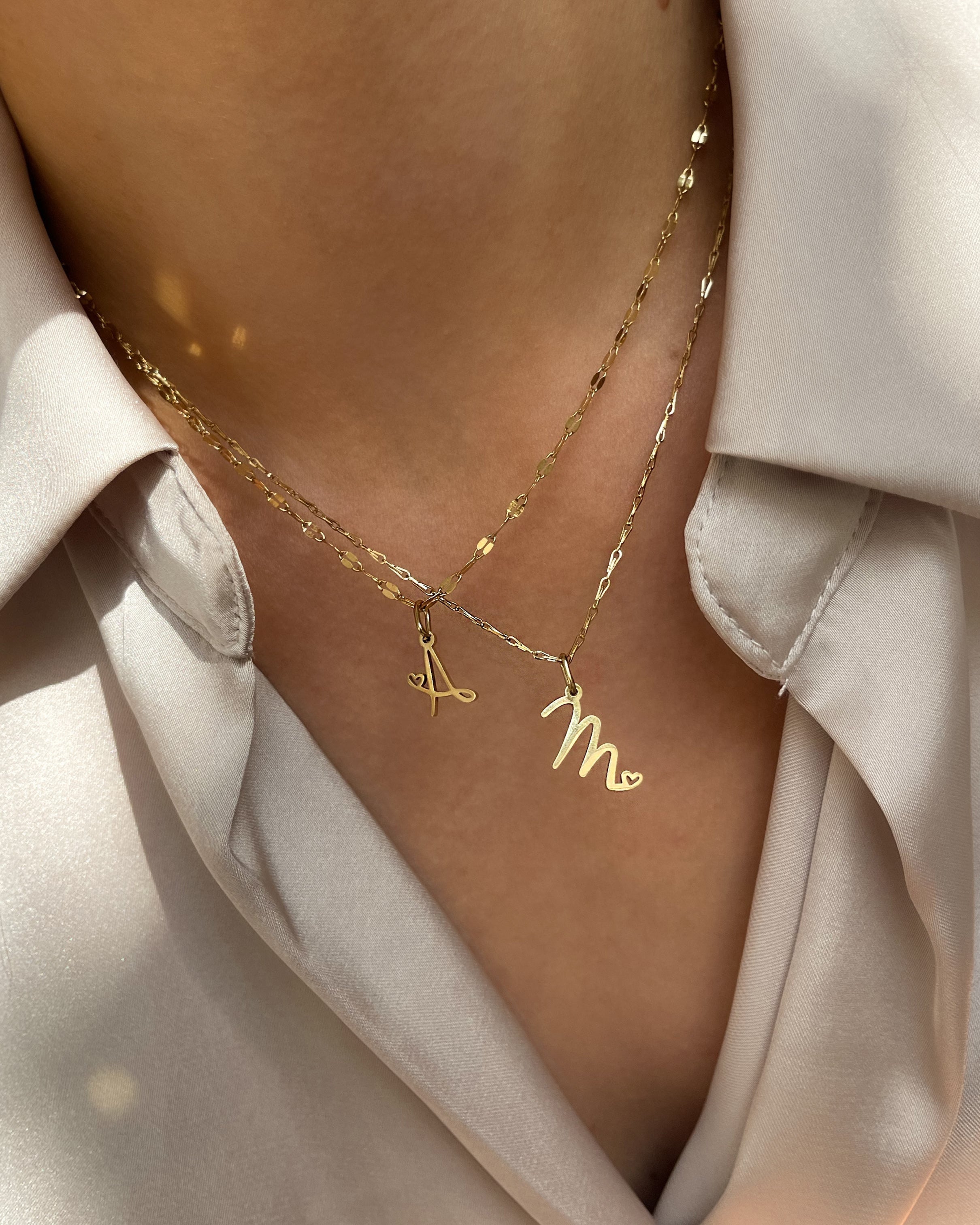 Vergoldeter Edelstahl Buchstaben Anhänger mit kleinem Herz Detail, getragen an filigraner Kette.