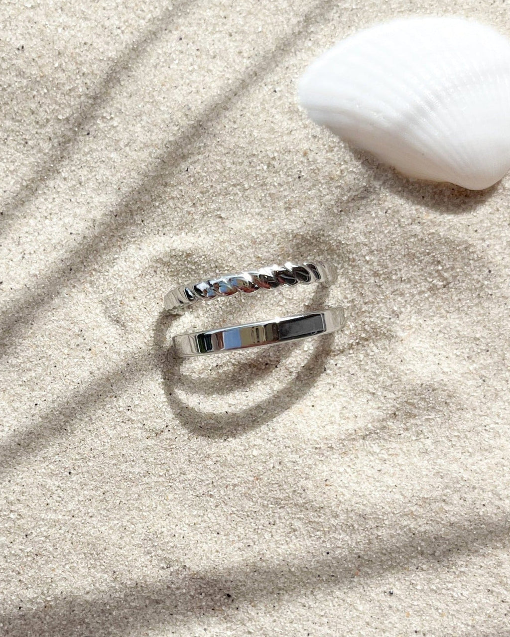 Doppellagiger, verstellbarer wasserfester Edelstahlring in silber im Sand.