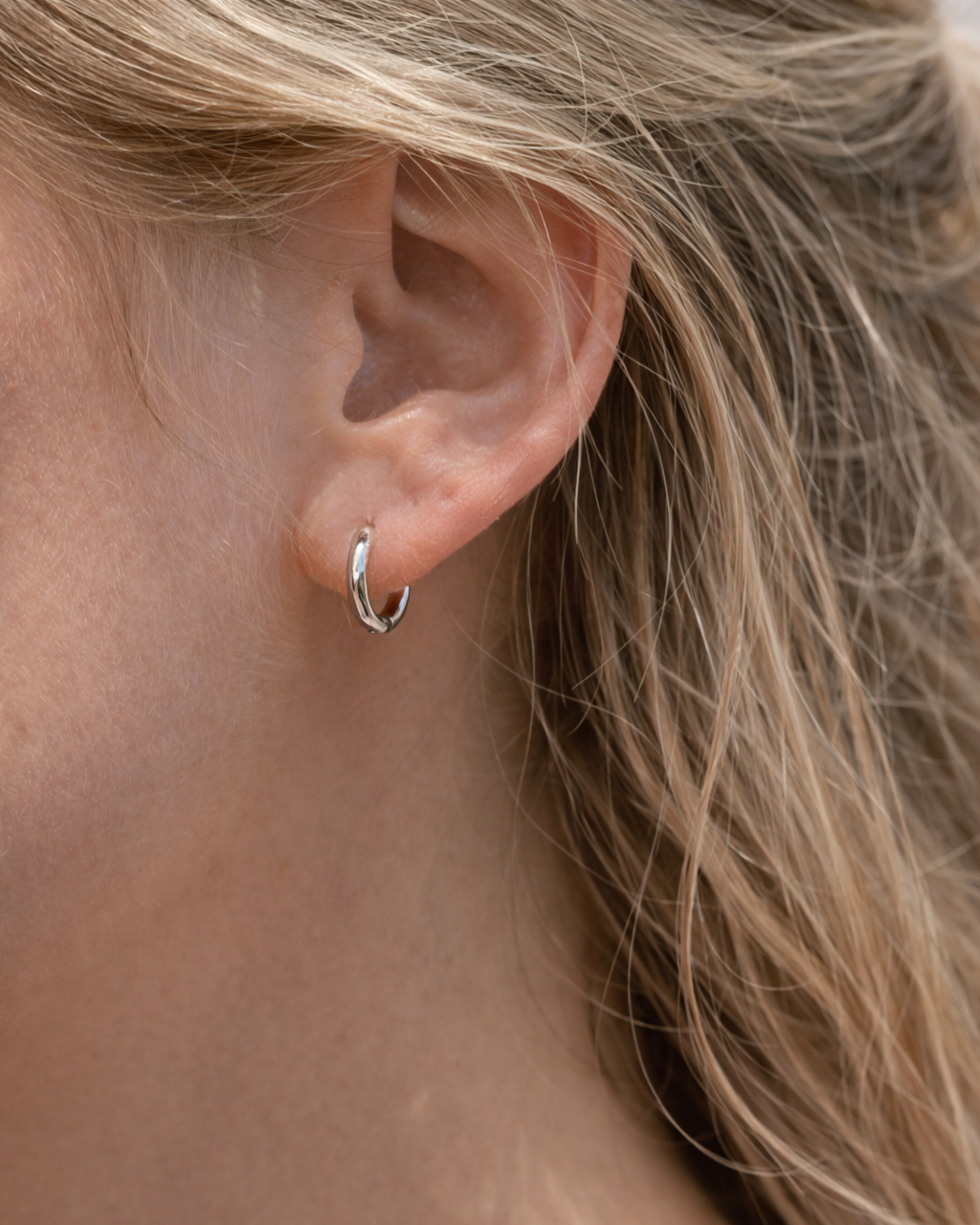 Dezente silberne Creolen im minimalistischen Look am Ohr. 