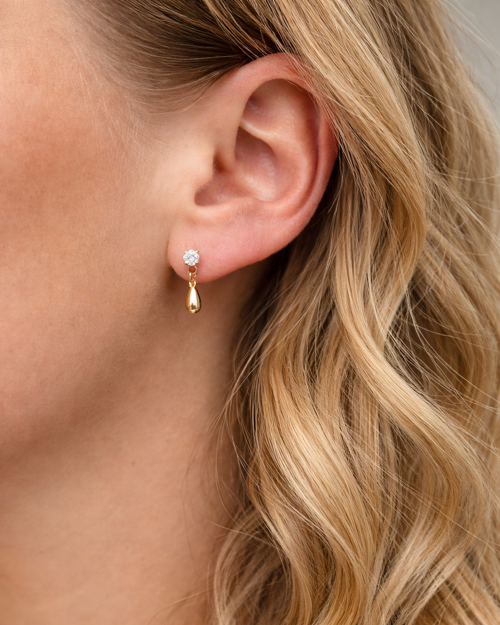 Goldene Sparkly Drop Ohrstecker mit Zirkoniastein am Ohr eines blonden Models Nahaufnahme