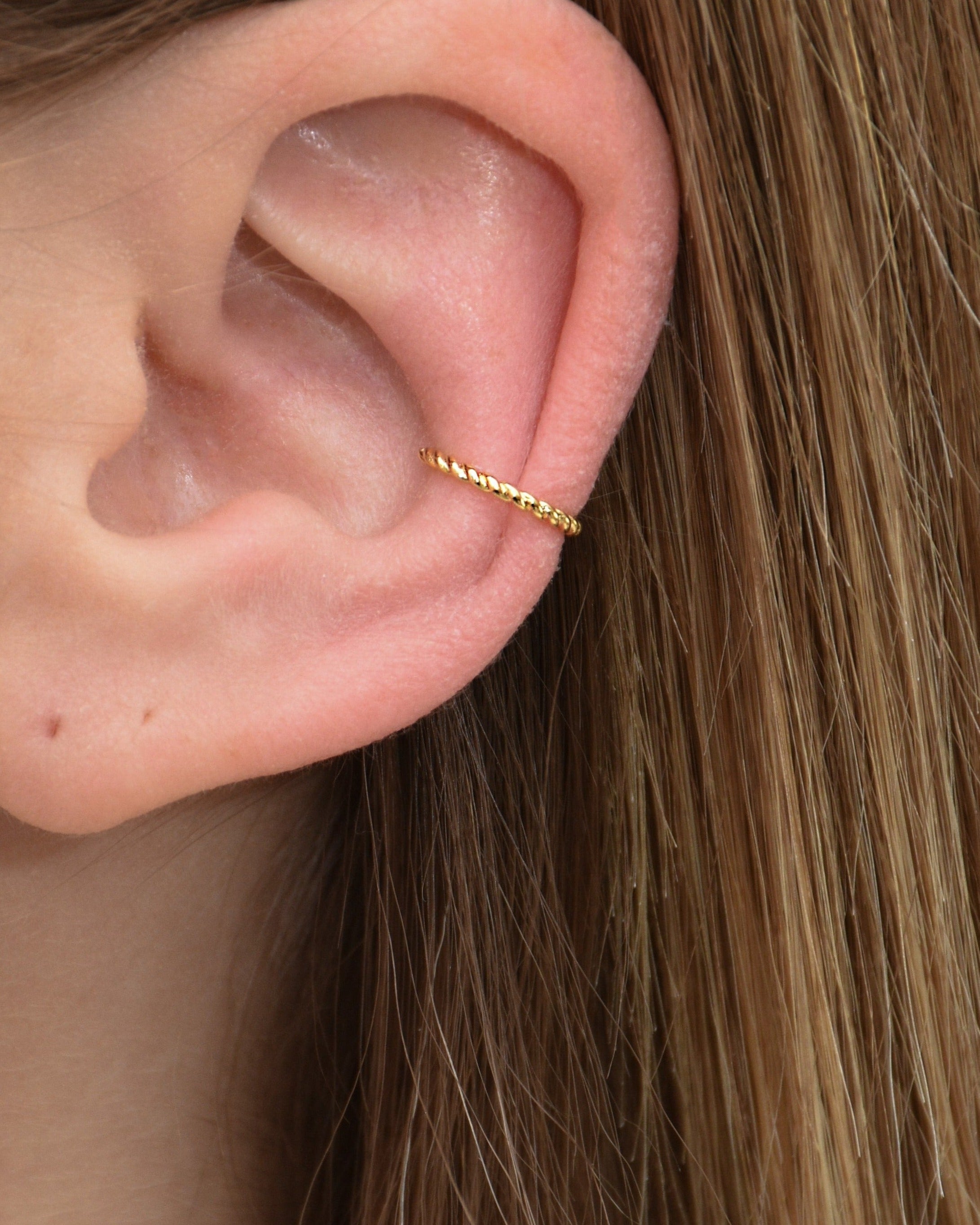 Feiner gedrehter Edelstahl Earcuff in gold getragen am Ohr.